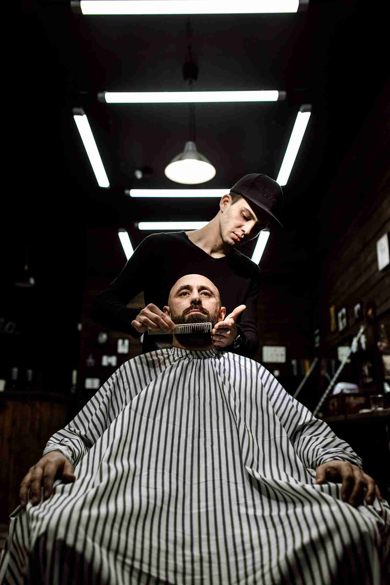 Professional barber detailing a client's beard in a luxury leather armchair.